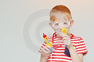 Mischievous boy playing doctor. Toy syringe, glasses and phonendoscope. Portrait