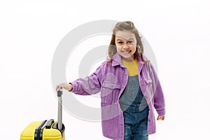 Mischievous traveler child, little girl going for holidays, posing with yellow suitcase on white background. Travel Trip