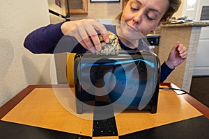 Misguided woman attempts to stuff a large blueberry scone into a small toaster slot, meant for bread