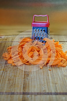 Mismatch: a large carrot next to a small grater. Cutting board on the kitchen table.