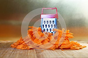 Mismatch: a small grater next to a large carrot. Cutting board on the kitchen table. Unusual mystery and optical illusion