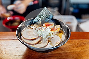 Miso Chashu Ramen: Japanese noodle in Miso soup with chashu pork, boiled egg, dry seaweed and chives in black bowl.