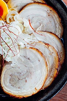 Miso Chashu Ramen: Japanese noodle in Miso soup with chashu pork, boiled egg, dry seaweed and chives in black bowl.