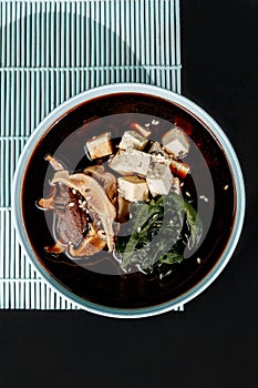 Miso soup classic with beef on blue pastel color plate at black background with sunlight and shadows, minimalism,top view