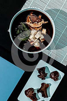 Miso soup classic with beef on blue pastel color plate at black background with sunlight and shadows, minimalism,top view