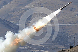 Missile launch with trail of smoke against mountain backdrop