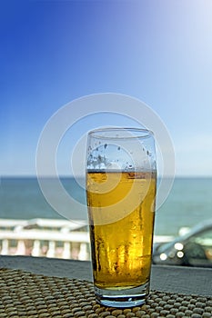 Misted glass of beer in the beach bar on the background of the sea landscape. Sunny hot day, afternoon.