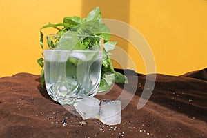 Misted glass of water on a hot Sunny day. juicy Basil, ice and a yellow wall