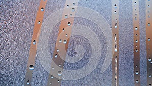 Misted glass of window with water drops falling down and blurred buildings at the background.