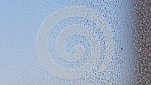 Misted glass of window with water drops texture and blue background. Selective focus.