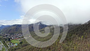 Misty clouds over green highlands covered summer forest and city at mountain foot. Fog covered green mountain peaks. Aerial view c