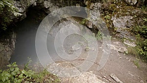 Misty entrance to dark cave. Stock footage. Mysterious and frightening cave entrance with fog and green plants around
