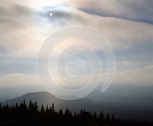 Misty evening of hilly area with ray of light.