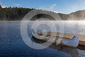 a boat dock in a misty lake with fog rising in the sky