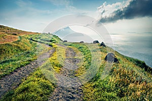 Misty morning view of Koltur Island. Bright summer scene of outskirts of Sydradalur village with old country road, Faroe Islands,