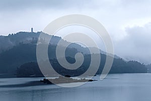 Misty mountains by Sun Moon Lake on a foggy morning, with a pagoda on the distant mountaintop under moody cloudy sky