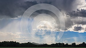 Misty rain and dark clouds in blue sky over field and trees