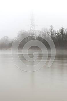 Misty river bank and electrical tower on a foggy morning, monochromatic scene