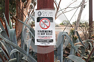 A black, red and white Warning, Do Not Drink Untreated Water sign on a rusty metal pole