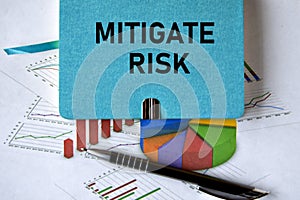 MITIGATE RISK - words on a green piece of paper on the background of a chart and a pen