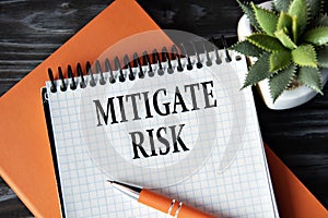 MITIGATE RISK - words in white notebook on dark wooden background with cactus and pen photo