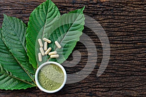 Mitragyna speciosa or kratom leaves with medicinal products in capsules and powder in white ceramic bowl and wooden table