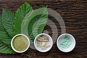 Mitragyna speciosa kratom leaves with medicine products in powder, capsules and tablet in white ceramic bowl with wooden texture