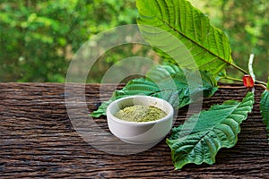 Mitragynina speciosa or Kratom leaves with powder product in white ceramic bowl on wood table photo