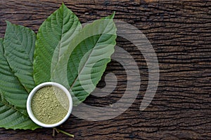 Mitragynina speciosa or Kratom leaves with powder product in white ceramic bowl and wooden table background