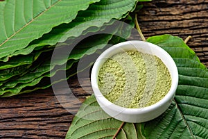 Mitragynina speciosa or Kratom leaves with powder product in white ceramic bowl and wooden table background
