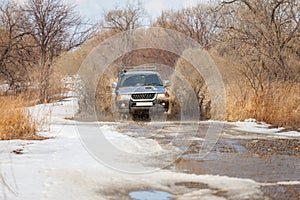 Mitsubishi Pajero Sport on dirt road in early spring making splashes from a puddle