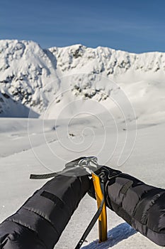 Mittens clipped carabiner on a yellow ice axe.