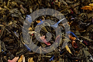 Mix of black tea with green sencha tea and cornflower flowers and strawberry slices.Dry fruit leaf texture background. Macro