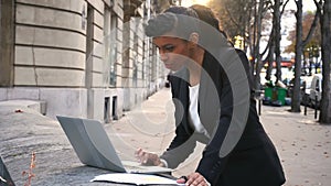 Mix blood secretary working with laptop in open air and reading papers.