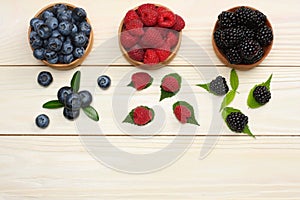 mix of blueberries, blackberries, raspberries in wooden bowl on light wooden table background. top view with copy space