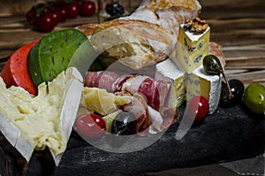 Mix cheese and meat on dark background on wood board with grapes, honey, nuts, tomatoes and basil. Top view.