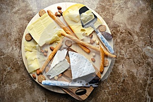 Mix of cheese on a wooden board on a marmur table. Grisini, nuts, brie, camembert, gouda, snack, date fruit, dessert for wine.