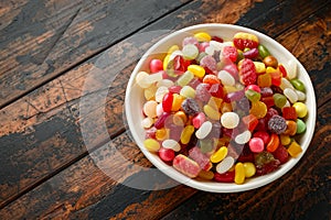 A mix of colorful candy in white bowl on wooden table