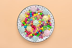 mix colorful sweets - white round plate with black peas, lollipop, meringue, chocolate, sprinkle on beige background Flat lay Top