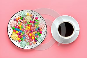 mix colorful sweets - white round plate with black peas, lollipop, meringue, chocolate, sprinkle, cup of coffee on gray background