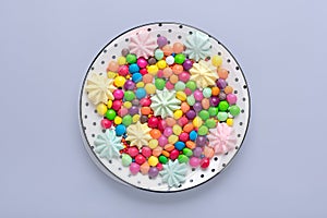 mix colorful sweets - white round plate with black peas, lollipop, meringue, chocolate, sprinkle on gray background Flat lay Top