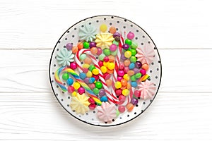 mix colorful sweets - white round plate with black peas, lollipop, meringue, chocolate, sprinkle on wooden background Flat lay Top