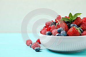 Mix of different fresh berries and mint in bowl on blue wooden table. Space for text