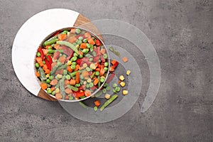 Mix of different frozen vegetables in bowl on grey table, top view. Space for text