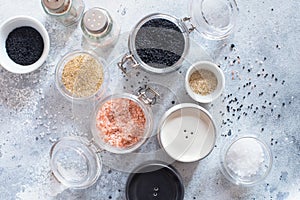 Mix of different salt types on grey concrete background. Sea salts, black and pink Himalayan salt crystals, powder. collection of