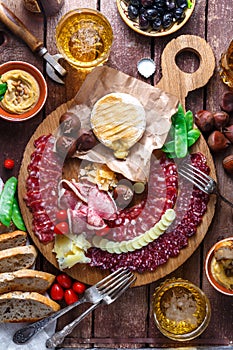 Mix of different snacks and appetizers: sausage, bread, olives, cheese, chestnuts, peas and beer on wooden board. Top