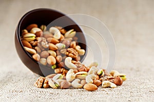 Walnut platter spilled out of the cup on the background of cloth from burlap. Nuts as structure and background, macro