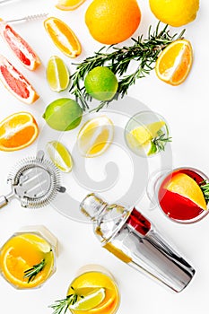 Mix exotic fruit cocktail with alcohol. Shaker and strainer near citrus fruits and glass with cocktail on white