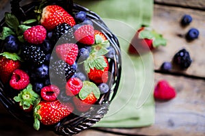 Mix of fresh berries in a basket on rustic wooden background