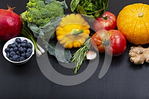 Mix of fresh healthy vegetarian ingredients of vegetables, fruit and berries on a black wooden background